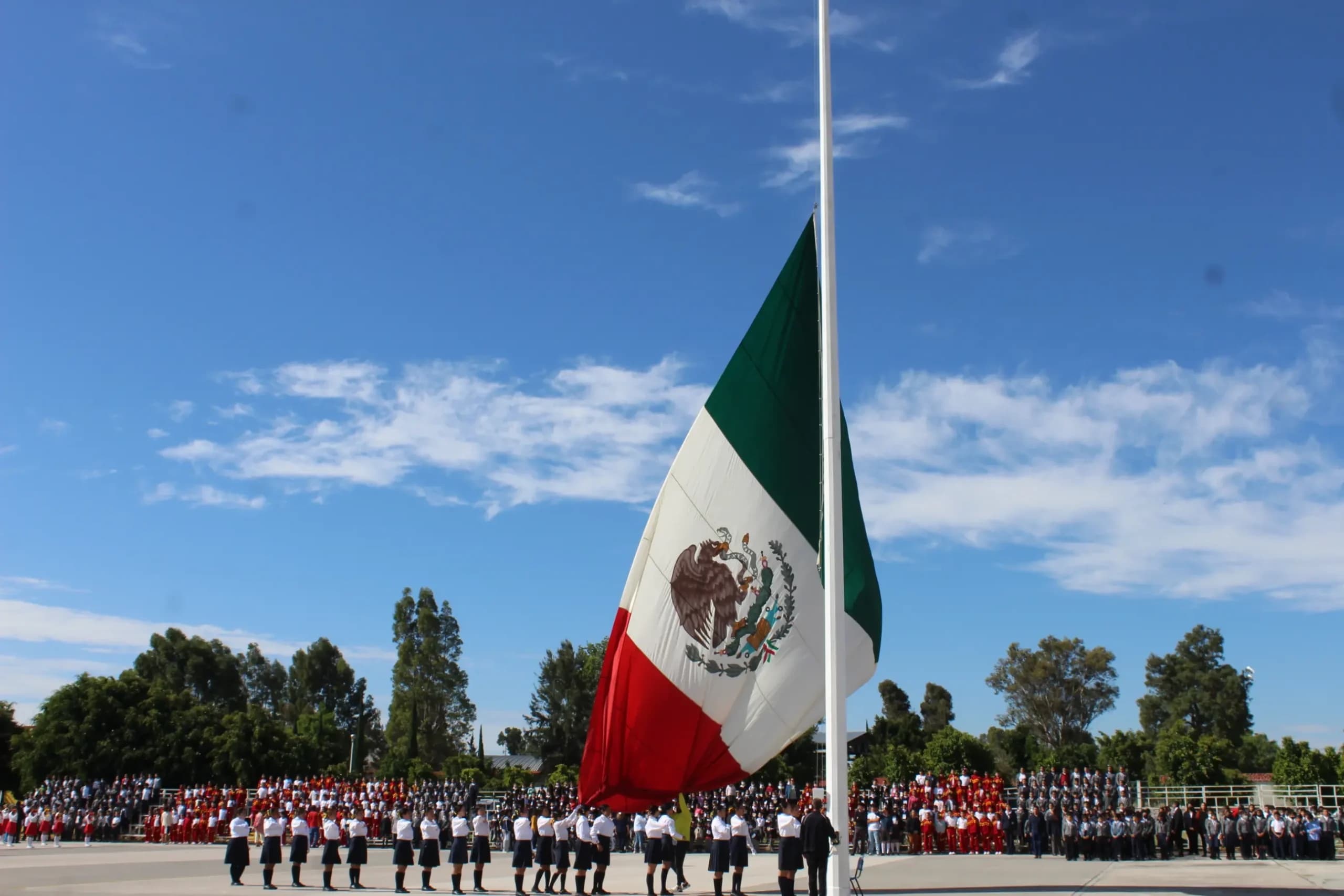 Ceremonia de honores a la bandera monumental en el Centro Escolar 5 de Mayo, con alumnos en formación bajo el cielo azul de Puebla